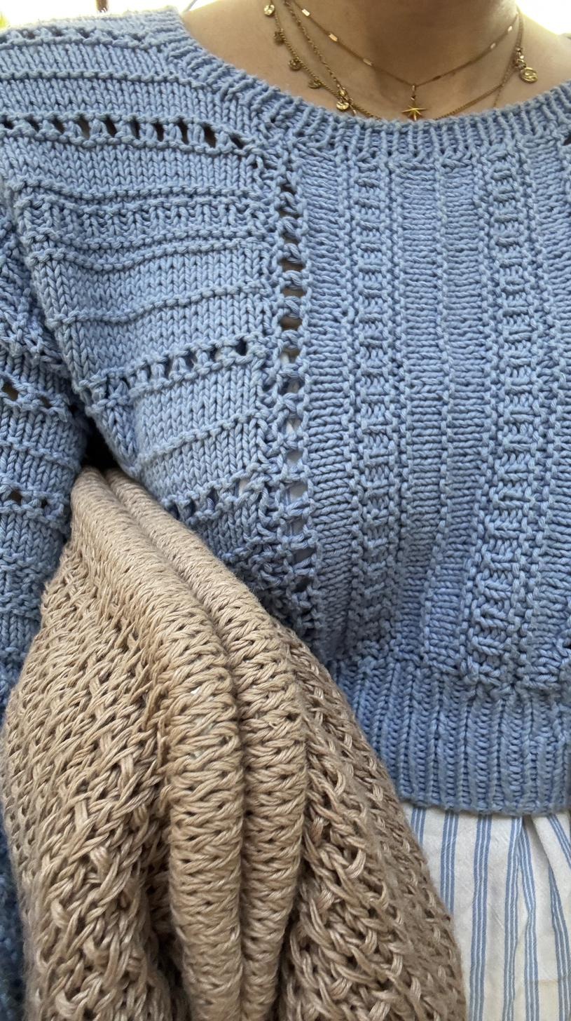 Close-up of a light blue knitted top showing textured stitch detail and an open lace panel