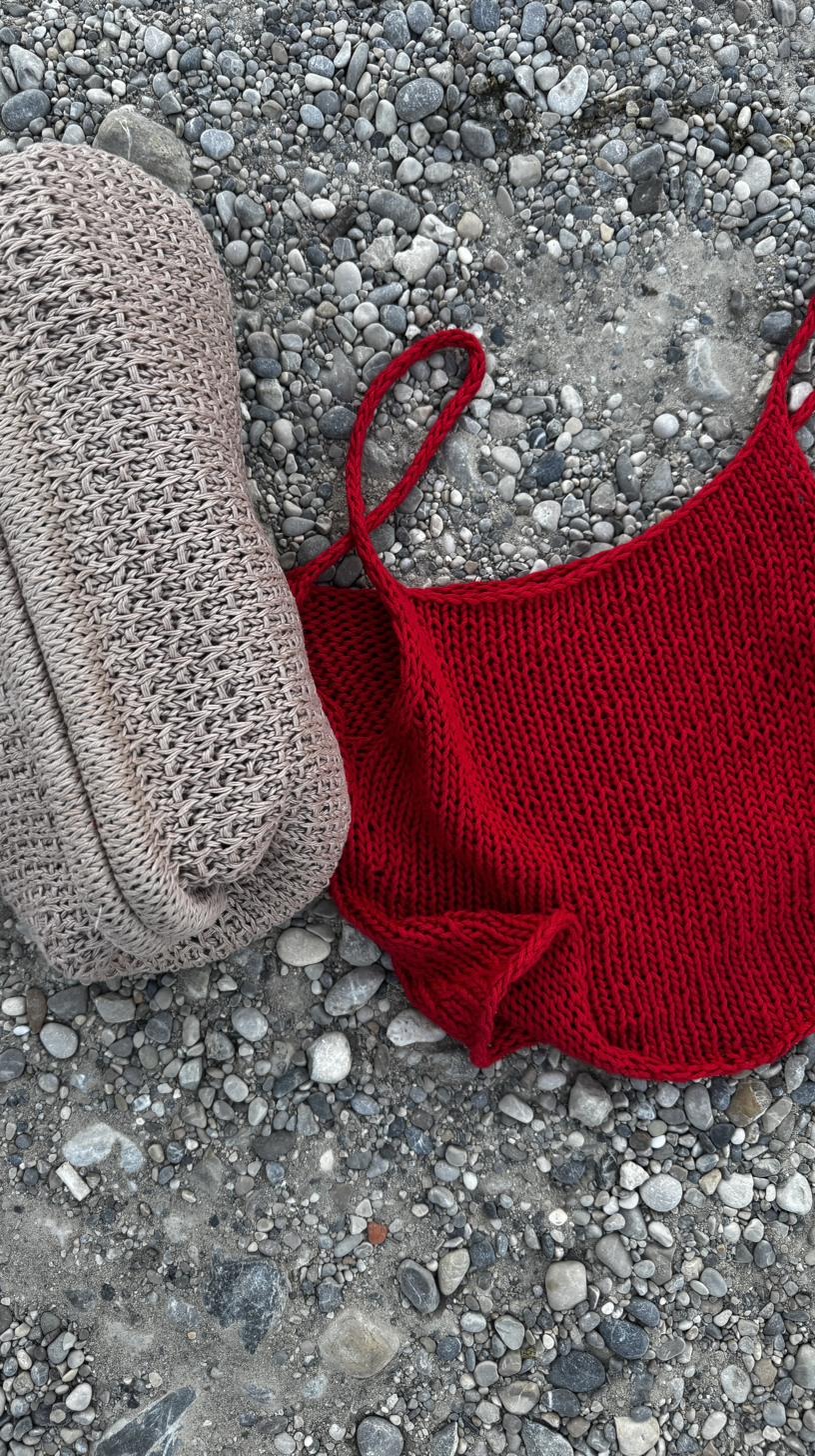 Deep red hand-knitted tote bag on a pebble beach